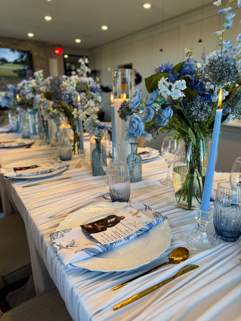 Blue floral tablescape with candlelight, layered place settings and glass vessels