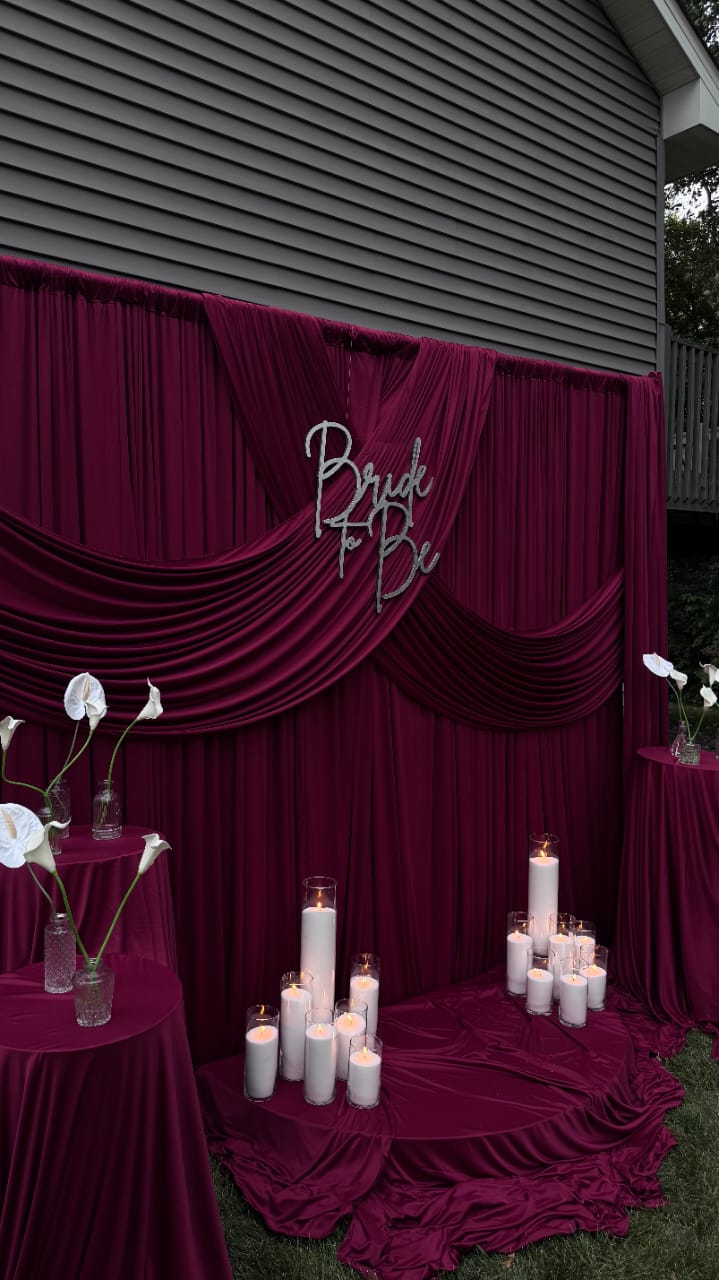 Burgundy draped wedding backdrop with candles and floral accents